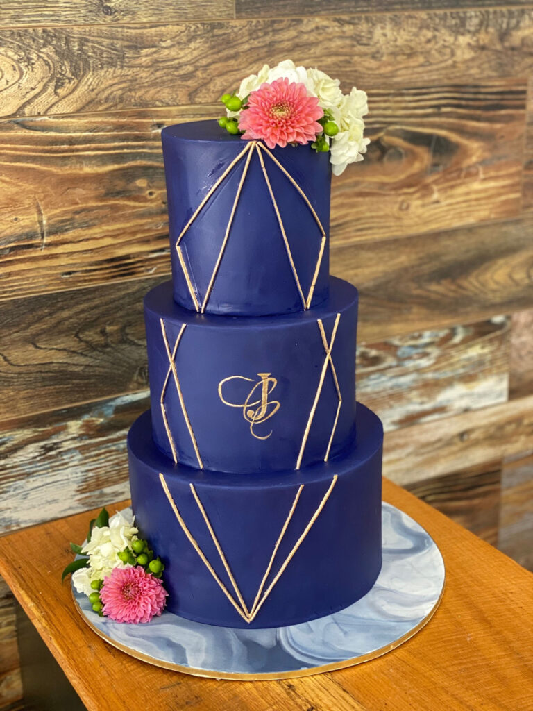Three tier navy cake with gold geometric lines and fresh flowers